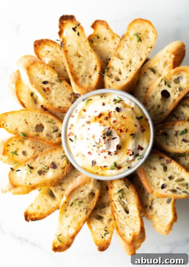 An appetizing close-up of a bowl of whipped ricotta, adorned with honey and crushed red pepper flakes, surrounded by perfectly toasted baguette slices, ready for a delightful bite.