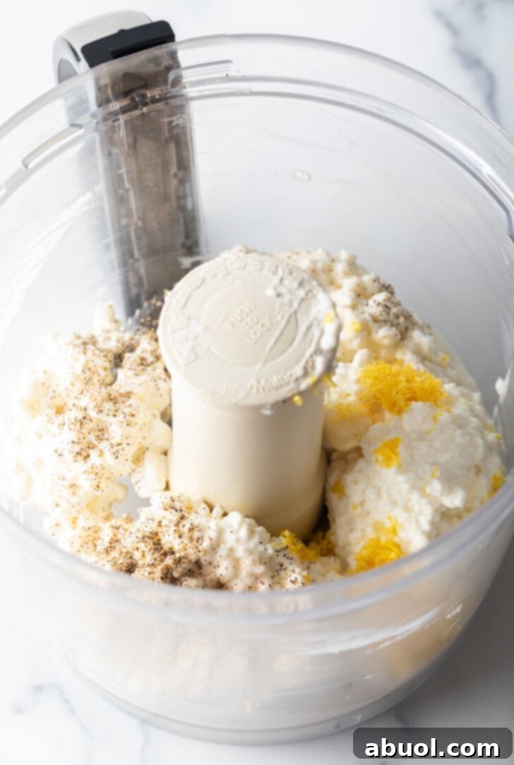 Close view of cottage cheese, lemon zest, and minced garlic in a food processor.