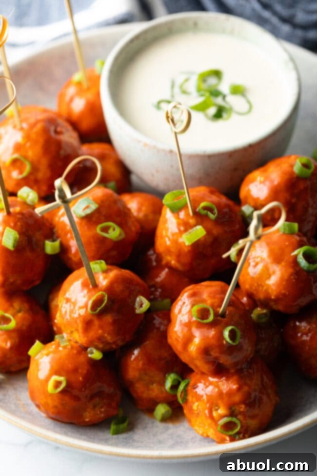 Plate of buffalo chicken meatballs skewered with serving toothpicks, nestled next to a white dish of ranch dressing dipping sauce.