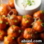 Plate of buffalo chicken meatballs skewered with serving toothpicks, nestled next to a white dish of ranch dressing dipping sauce.