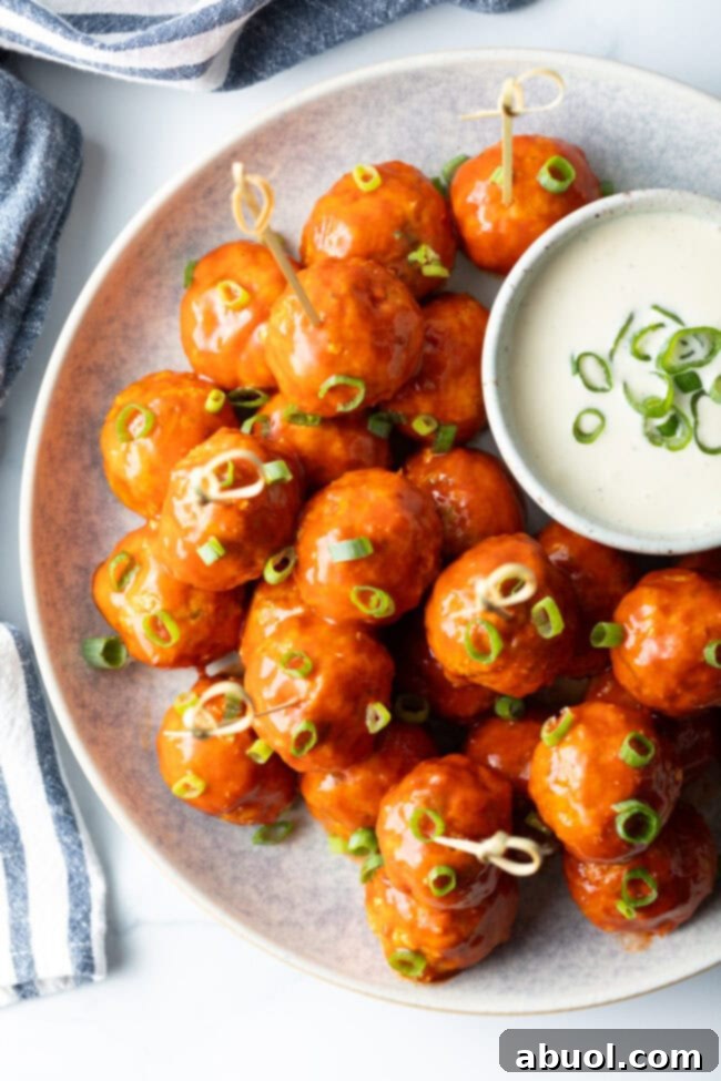 Plate of buffalo chicken meatballs skewered with serving toothpicks, nestled next to a white dish of ranch dressing dipping sauce.