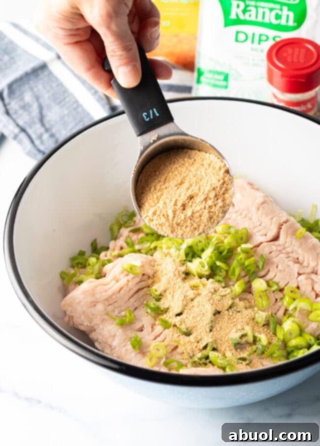Hand with a 1/2 measuring cup adding breadcrumbs to white mixing bowl.