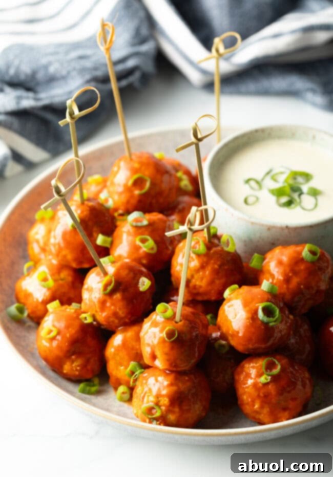 Plate of buffalo chicken meatballs skewered with serving toothpicks, nestled next to a white dish of ranch dressing dipping sauce.