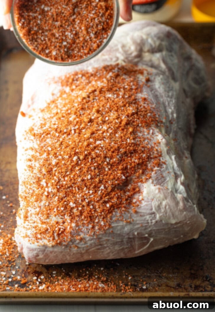 Raw pork shoulder covered in mayonnaise and heavy sprinkling of dry spice rub.