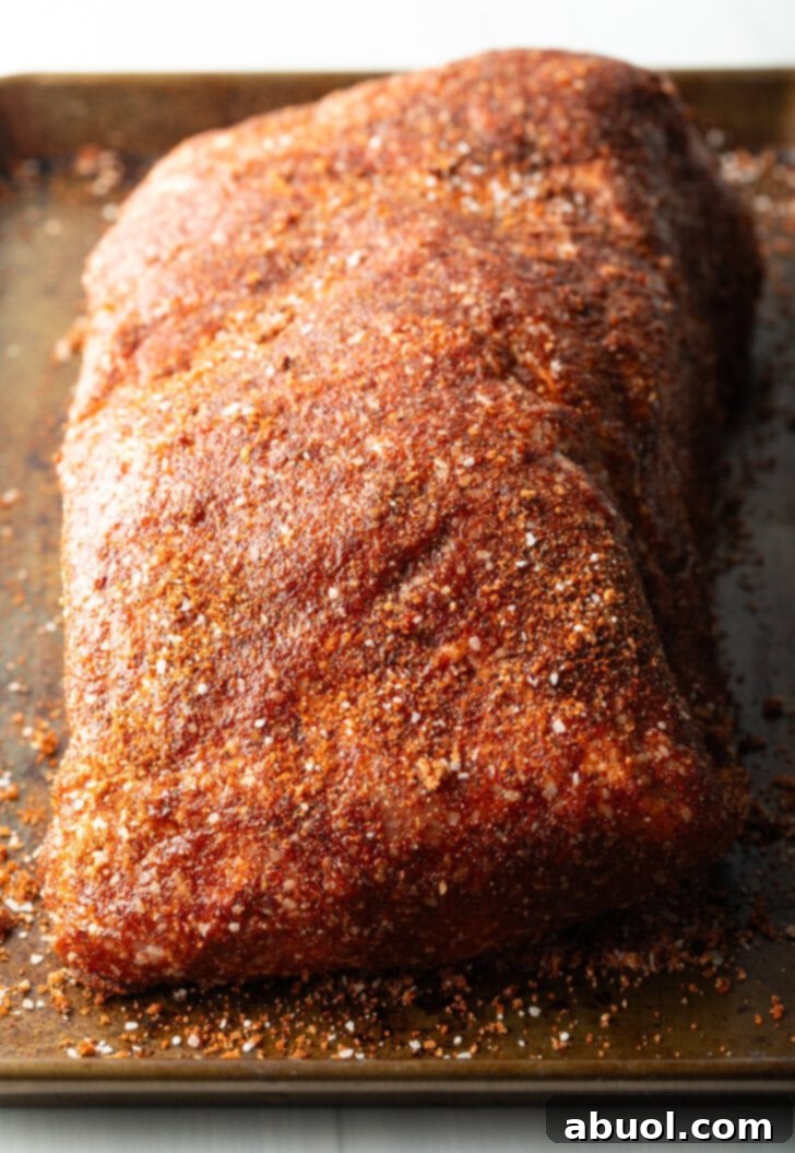 Raw pork shoulder covered in mayonnaise and heavy sprinkling of dry spice rub.