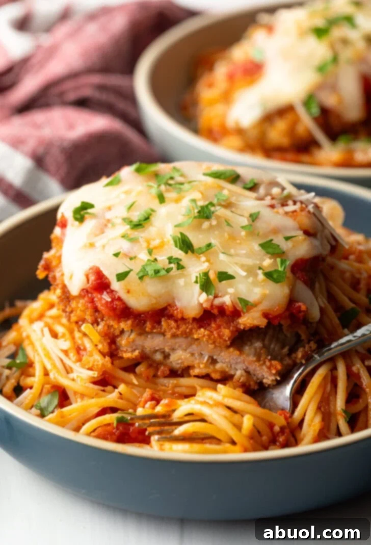 A cutlet of veal parmesan on top of spaghetti. A bite has been removed from the veal to show the juicy inside.