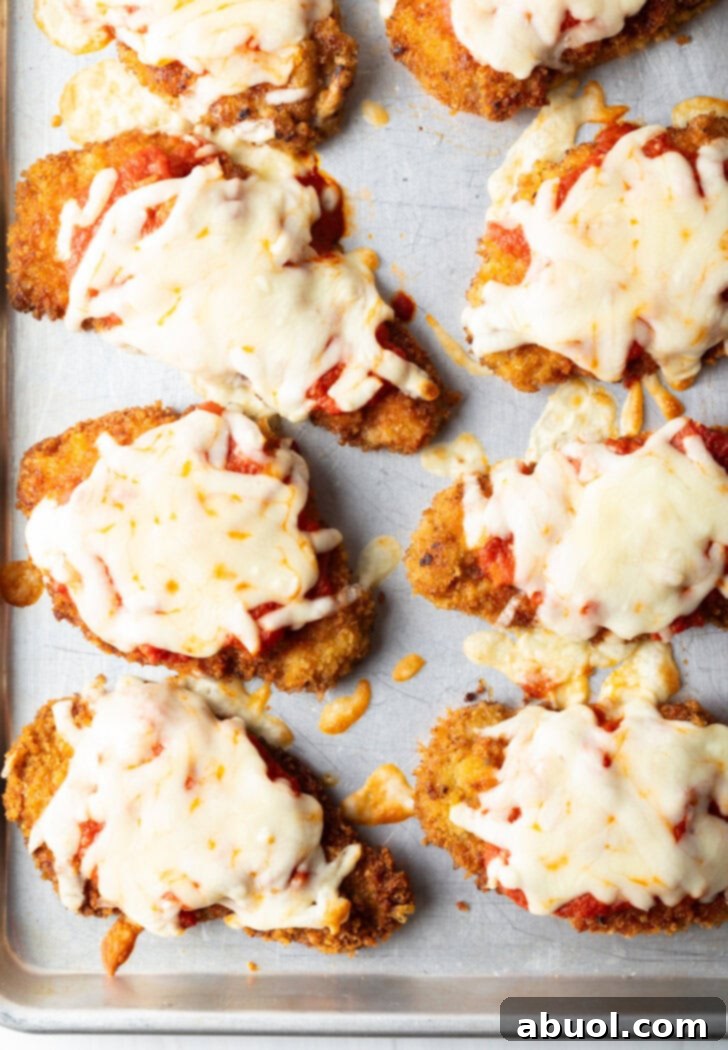 Top down view of 6 pieces of breaded baked veal on a baking sheet, topped with melted mozzarella cheese