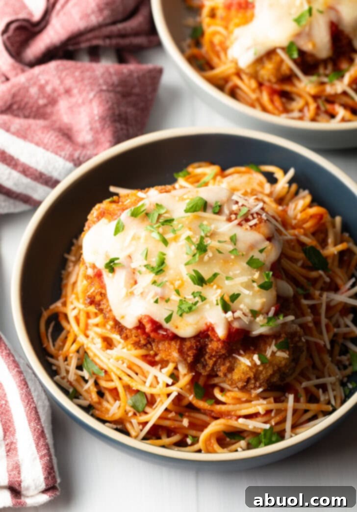 Breaded fried veal parmesan on top of spaghetti in a blue pasta bowl.