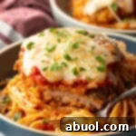 A cutlet of veal parmesan on top of spaghetti. A bite has been removed from the veal to show the juicy inside.