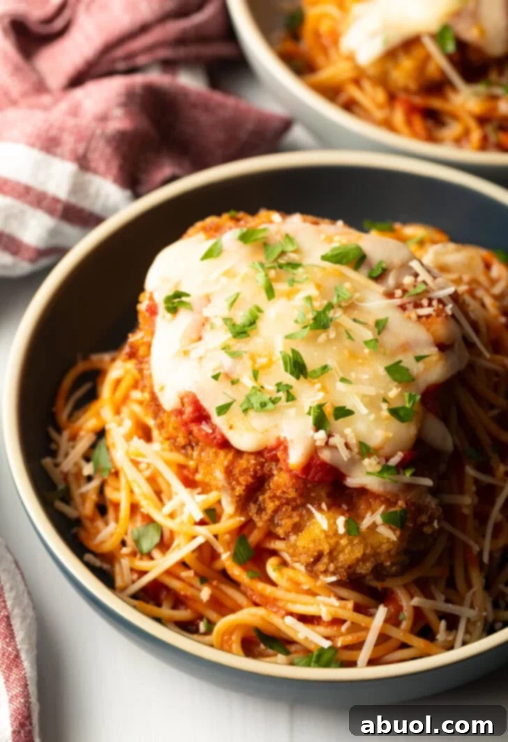 Breaded fried veal parmesan on top of spaghetti in a blue pasta bowl.