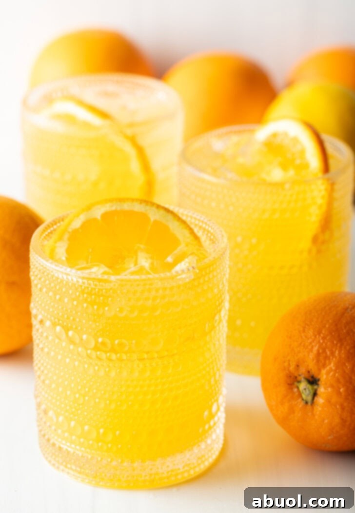 Ultimate Orange Crush Cocktail 11 Two orange crush drinks in glasses, each garnished with a slice of orange. There are fresh oranges and lemons around the glasses.