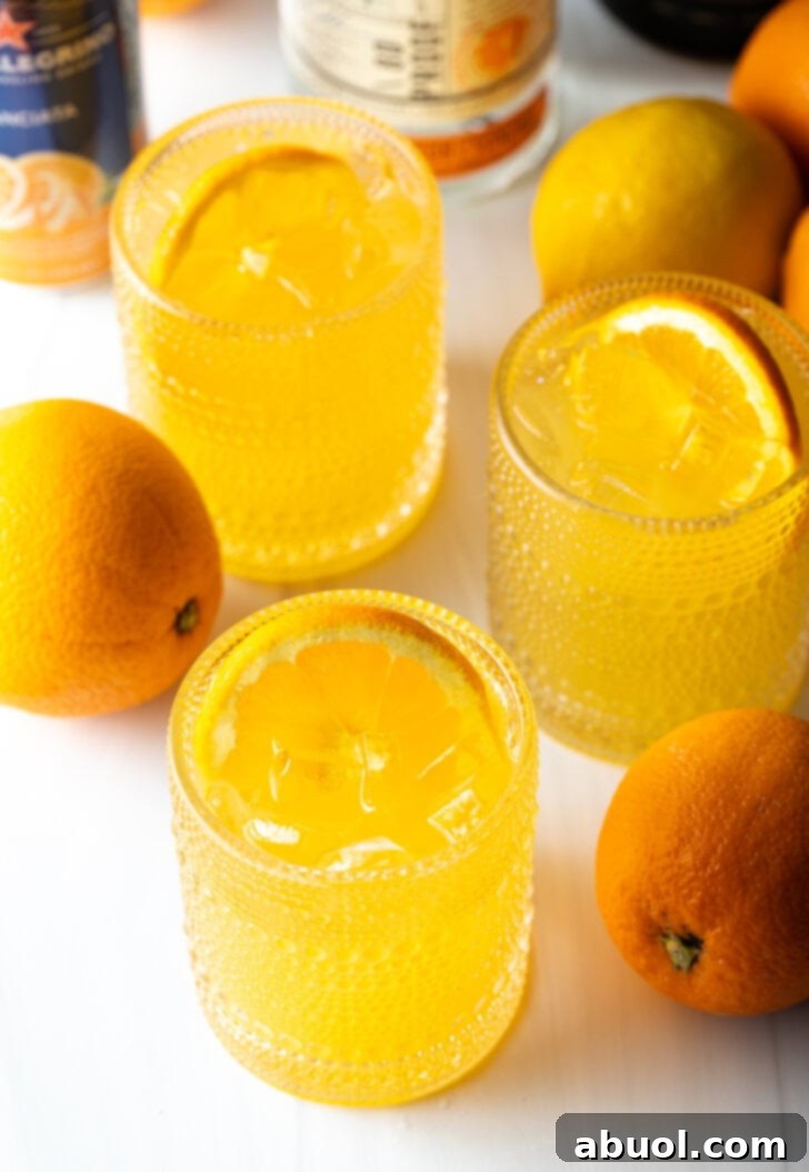 Ultimate Orange Crush Cocktail 12 Three orange crush cocktails in glasses, each garnished with a slice of orange. There are fresh oranges and lemons around the glasses.