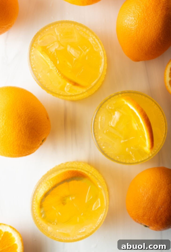 Ultimate Orange Crush Cocktail 3 Top down view 4 orange crush drinks in glasses, each garnished with a slice of orange. There are fresh oranges and lemons around the glasses.