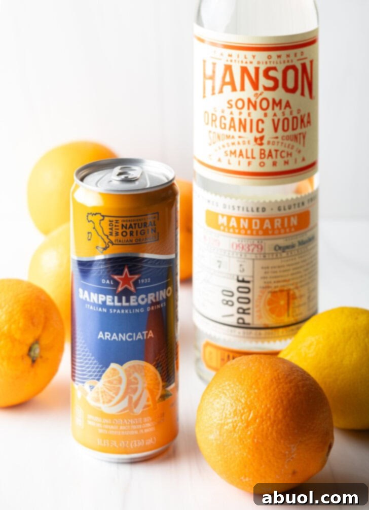 Ultimate Orange Crush Cocktail 4 Can of orange soda, bottle of vodka, several fresh oranges and lemons all around.