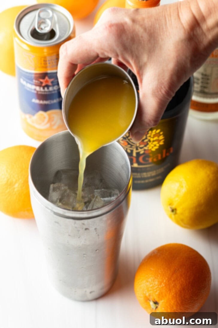 Ultimate Orange Crush Cocktail 7 Hand adding orange juice from metal glass into a metal shaker.