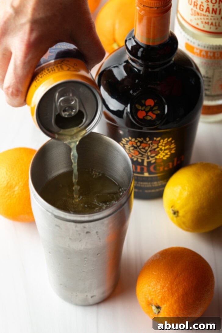 Ultimate Orange Crush Cocktail 8 Hand pouring orange soda into metal cocktail shaker.