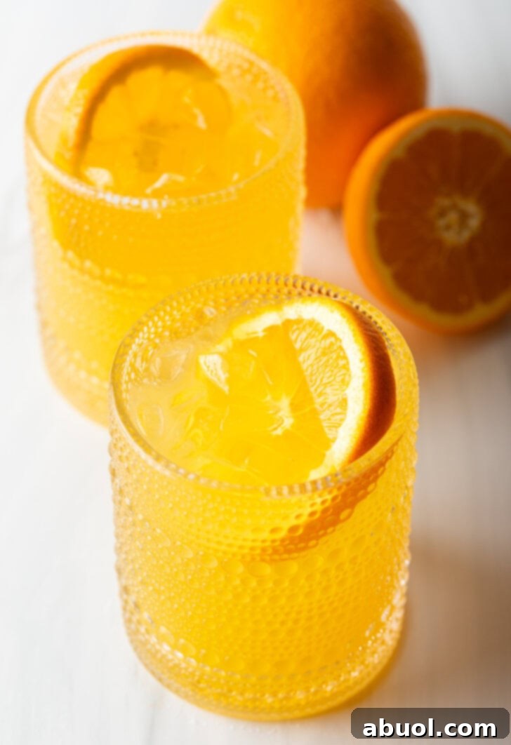 Ultimate Orange Crush Cocktail 10 Two orange crush cocktails in glasses, each garnished with a slice of orange. There are fresh oranges and lemons around the glasses.
