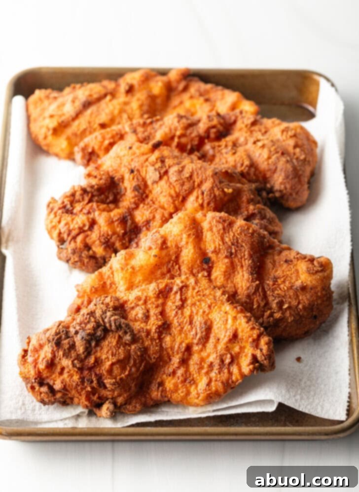 Perfectly fried chicken cutlets resting on a tray, golden brown and crispy, ready to be assembled into delicious sandwiches.