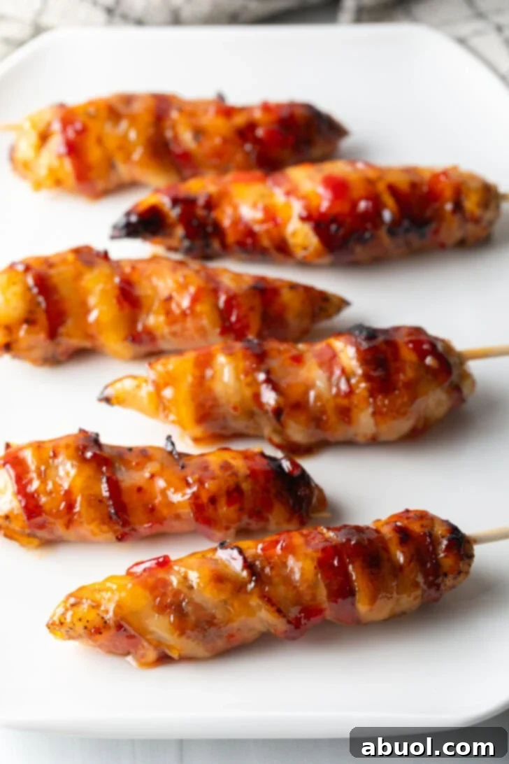 Mouthwatering Bacon-Wrapped Chicken 2 6 skewered bacon wrapped chicken tenders coated with hot sauce on a white plate.