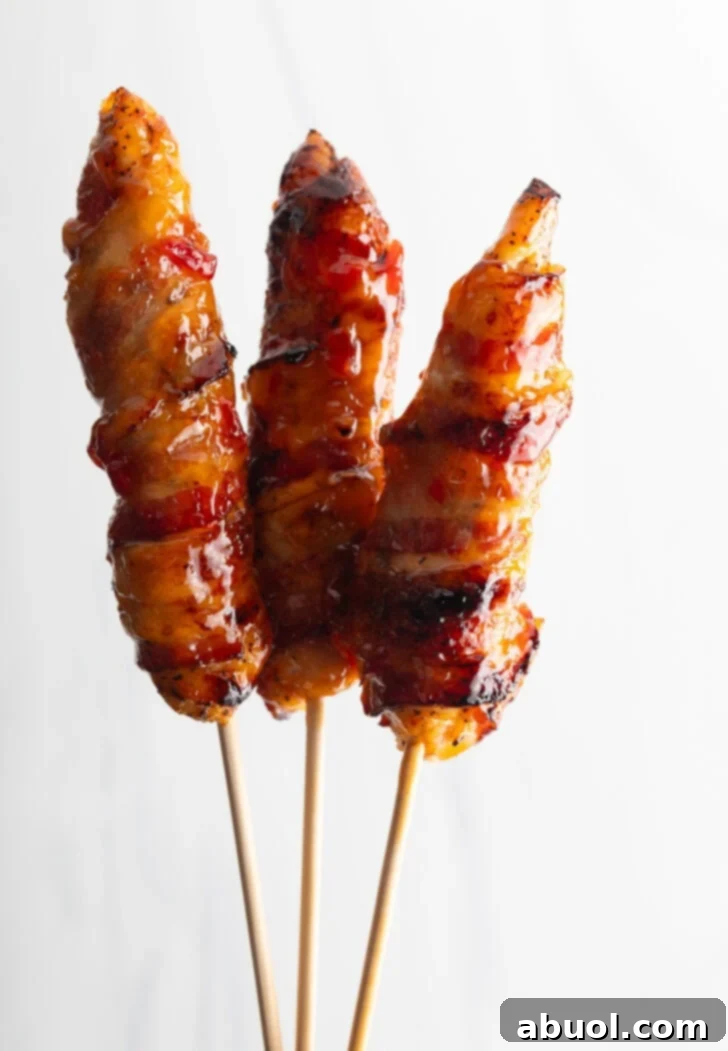 Mouthwatering Bacon-Wrapped Chicken 3 3 bacon wrapped hot sauce coated chicken skewers held up vertically to camera.