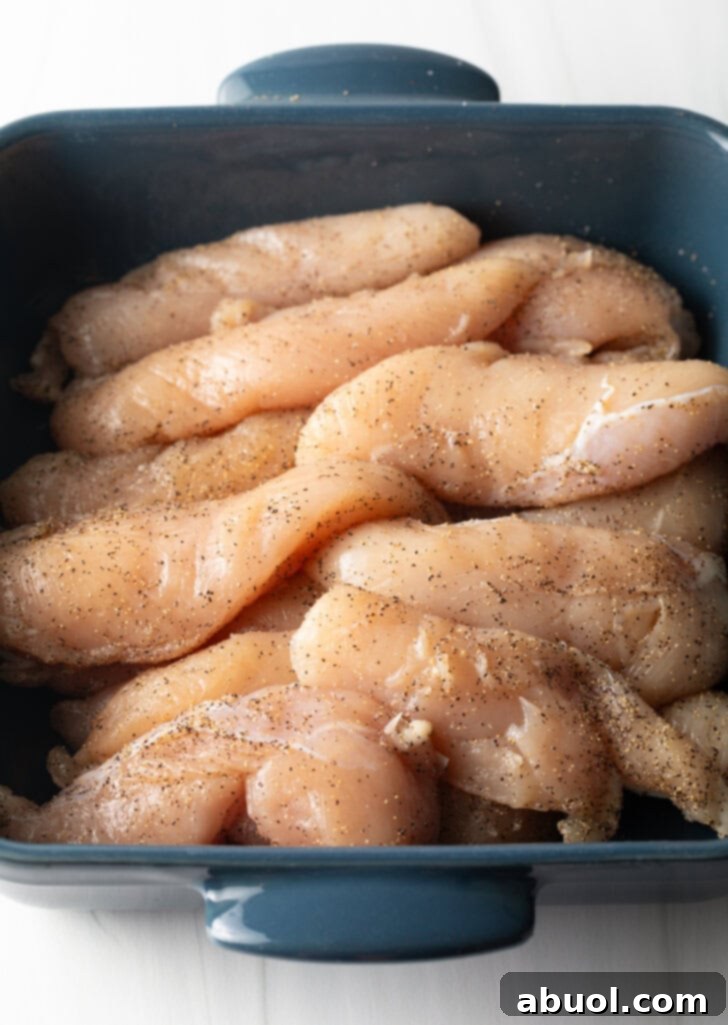 Mouthwatering Bacon-Wrapped Chicken 5 Square blue baking dish filled with raw chicken breast tenders.