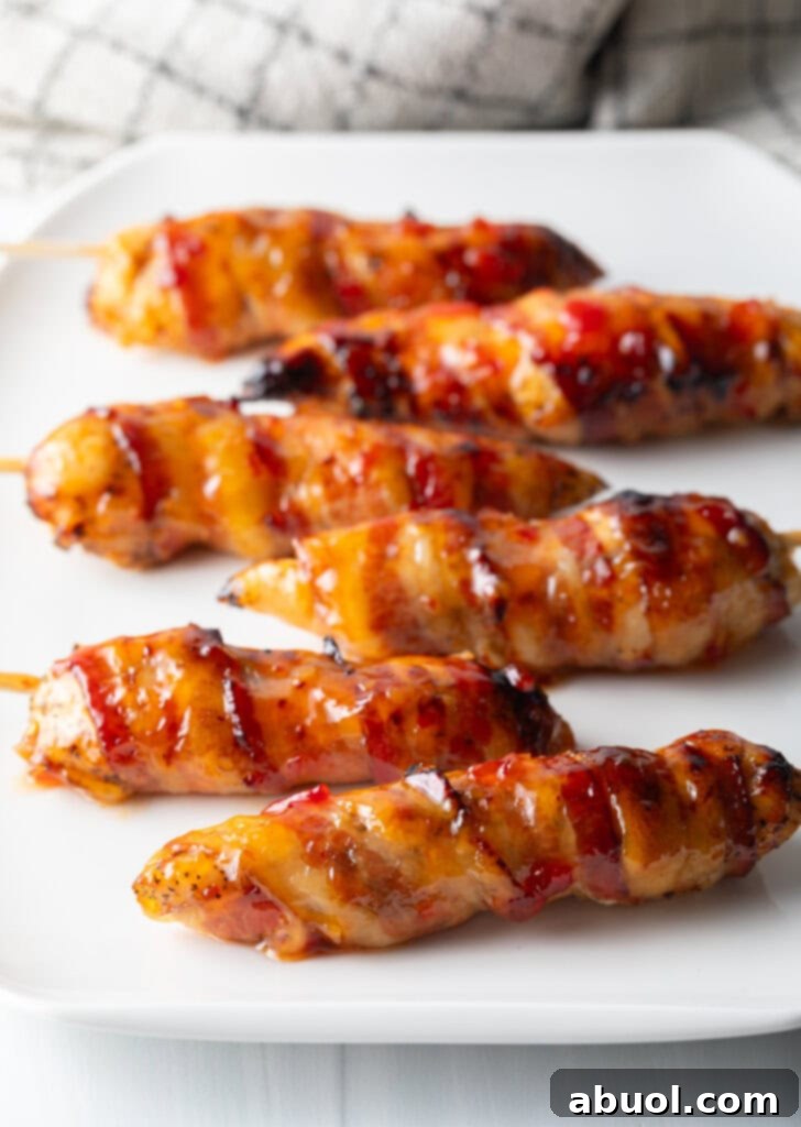 Mouthwatering Bacon-Wrapped Chicken 9 6 skewered bacon wrapped chicken tenders coated with hot sauce on a white plate.