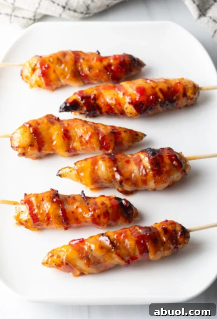 Mouthwatering Bacon-Wrapped Chicken 10 Top down view 6 skewered bacon wrapped chicken tenders coated with hot sauce on a white plate.