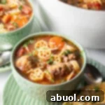 A vibrant green bowl filled with Italian meatball soup, showcasing wheel-shaped pasta, thinly sliced carrots, and perfectly browned meatballs in a rich, deep red tomato broth.