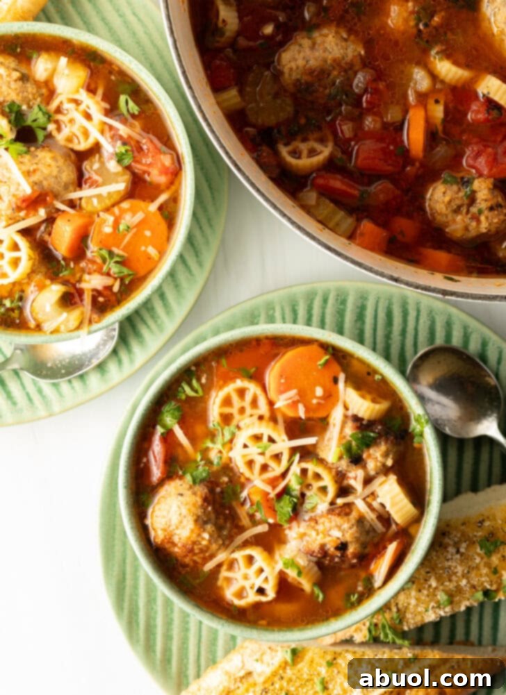 A top-down view of two inviting green bowls of Italian meatball soup, generously filled with wagon wheel pasta, bright orange carrot slices, and savory meatballs submerged in a rich tomato broth.