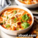 No-Fuss Lasagna Soup 9 White bowl loaded with lasagna soup, garnished with two fresh basil leaves. A slice of baguette is on a white plate under the bowl.