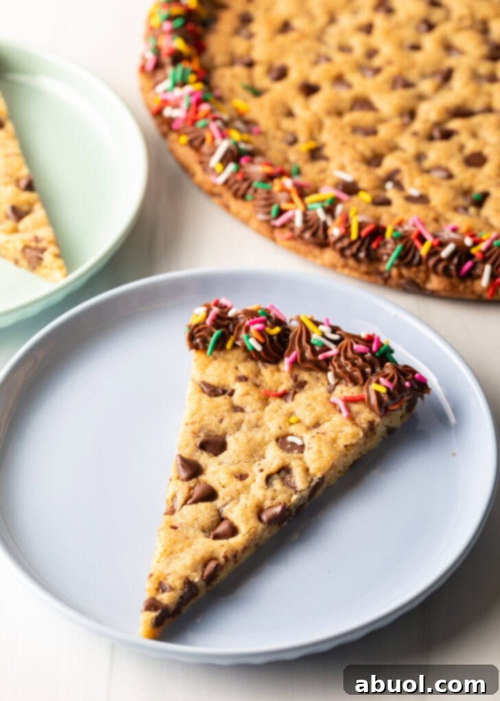A single, perfectly cut triangle slice of homemade cookie cake rests invitingly on a pastel blue plate, showcasing its golden-brown edges and soft, chocolate-studded interior.
