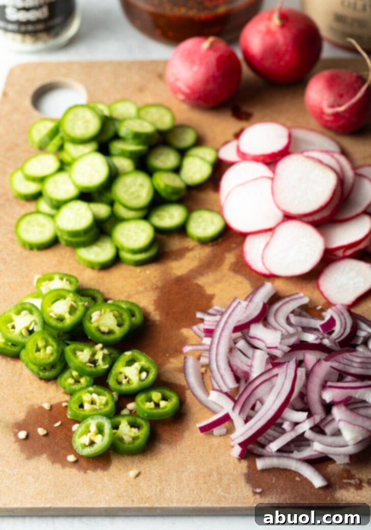 Crudo garnishes prepped on a cutting board: Individual piles of sliced cucumbers, radishes, jalapenos, and red onion.