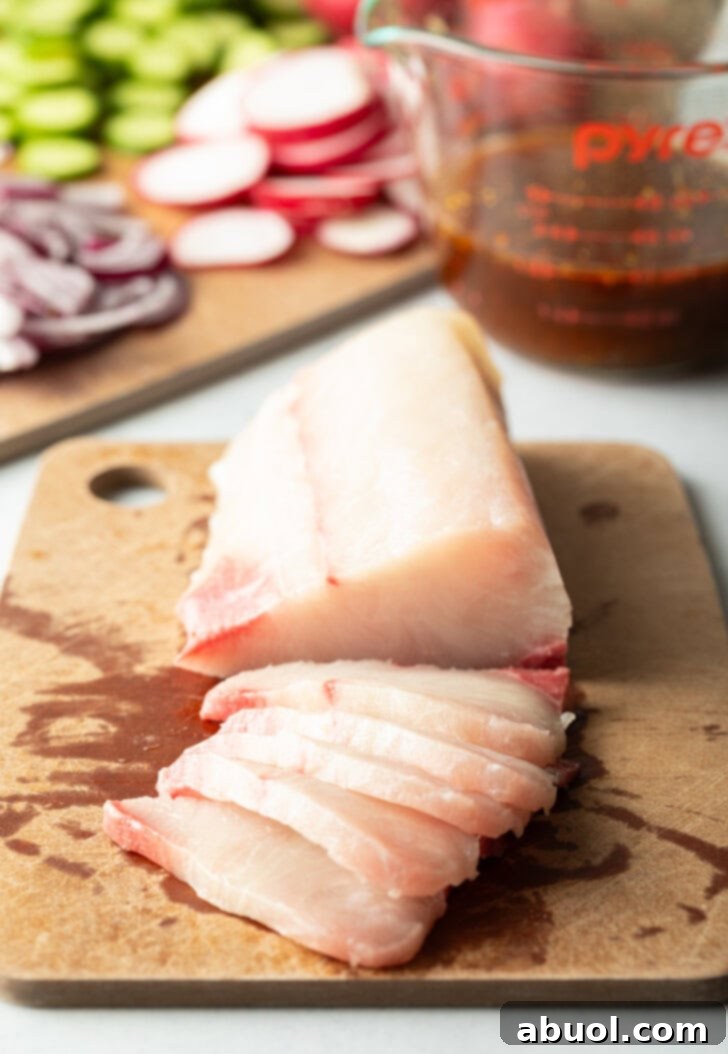 Large fillet of hamachi on a cutting board, front half of the fish is cut into thin slices.