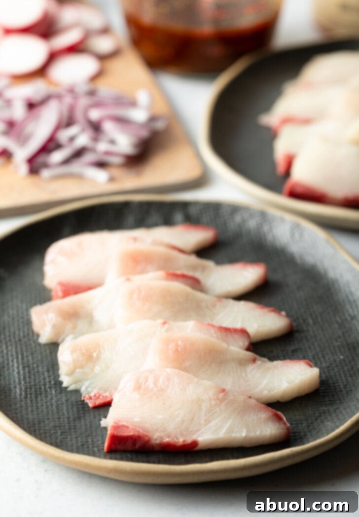 4 pieces of hamachi on a black oval plate.