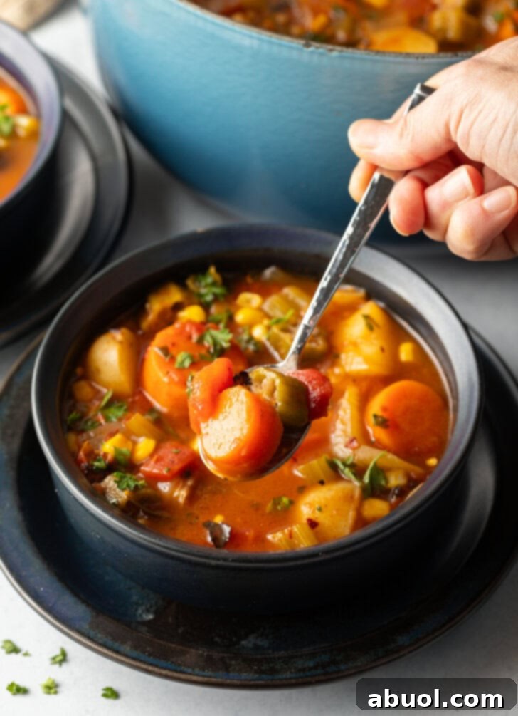 Metal spoon holding a spoonful of vegetable soup to camera over a black bowl.