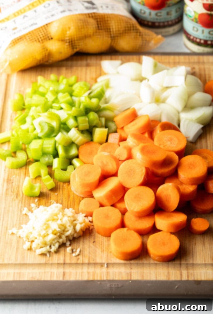Recipe ingredients on a wood cutting board. Piles of sliced carrots, chopped onion and celery, and minced garlic.