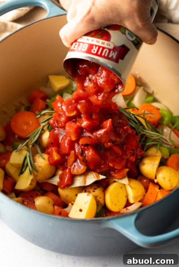 Hand adding canned diced tomatoes to the pot with fresh veggies.