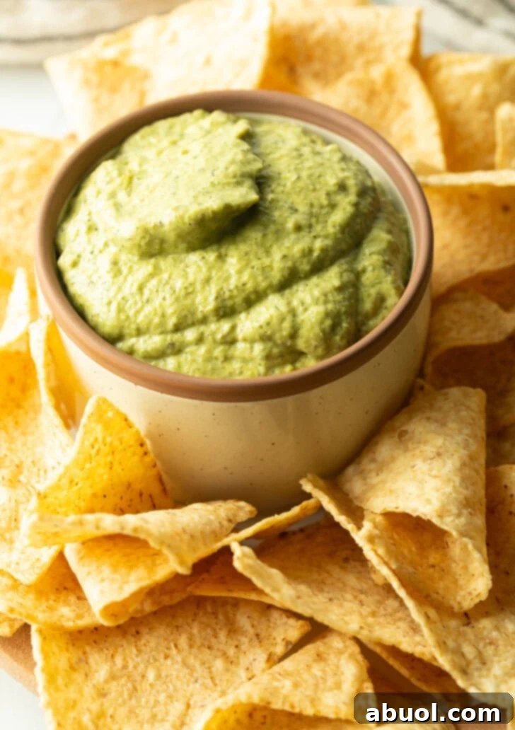 Small bowl of poblano cream sauce surrounded by tortilla chips.