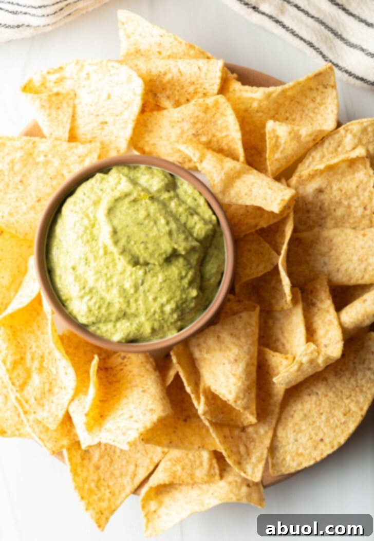 Top down small bowl of poblano cream sauce surrounded by tortilla chips.