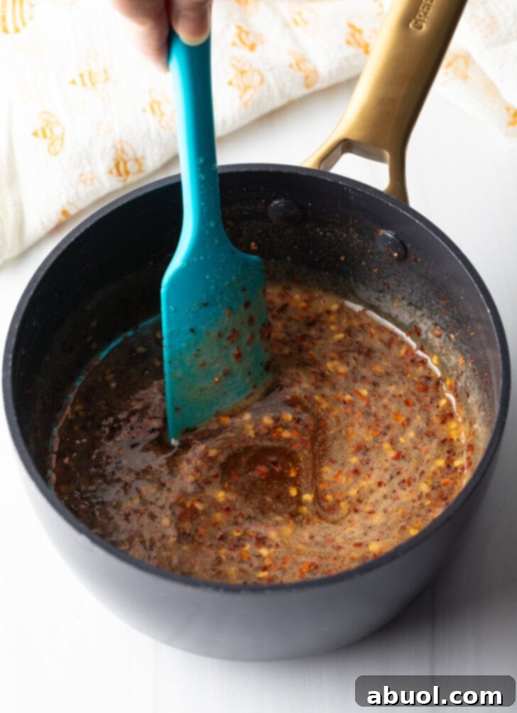 Sweet Heat Honey Blend 7 Blue spatula stirring mixture in a black sauce pot.