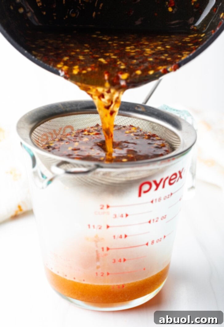 Sweet Heat Honey Blend 8 Pouring mixture from the black sauce pot into a metal sieve over a glass measuring cup.