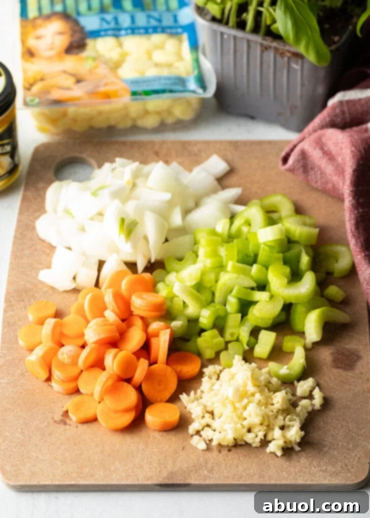 Soup recipe ingredients: Individual chopped piles of carrots, celery, onion, and garlic on a cutting board.