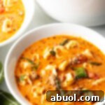 Top down view of a white bowl with creamy sausage and tortellini soup. The large pot of soup is off to the side.
