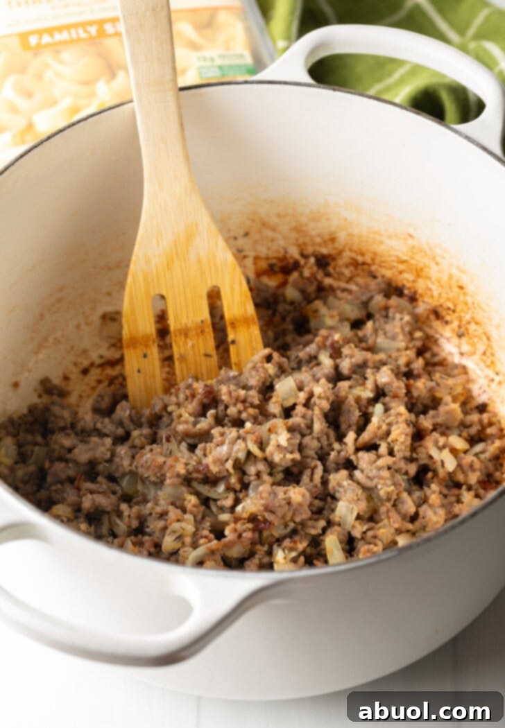 A large white cooking pot with ground browned sausage and a wooden spoon, ready for the next ingredients.