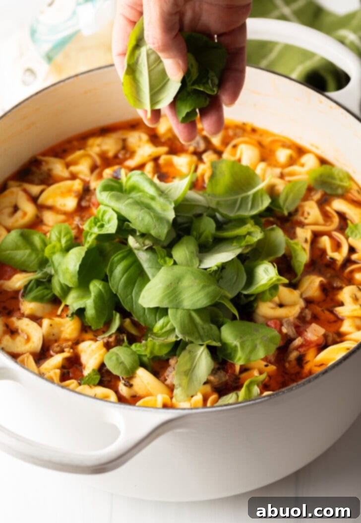 A hand gently adding fresh basil leaves to the finished soup, ready to be stirred in.