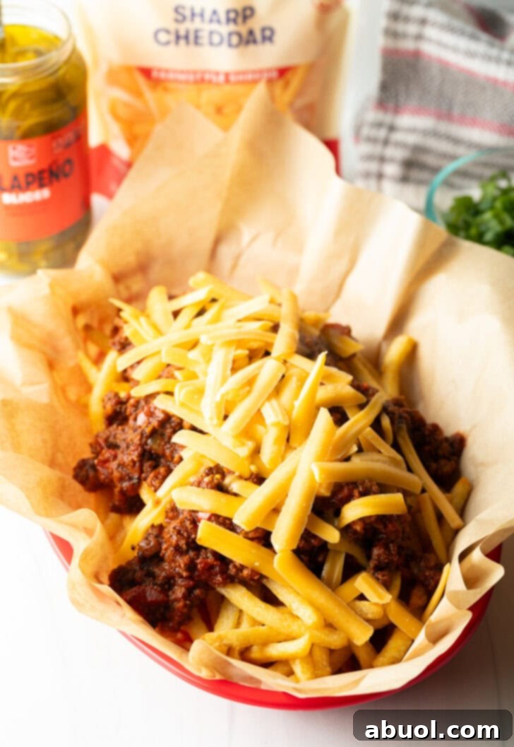 Basket with parchment paper, filled with crispy fries topped with chili and shredded cheddar cheese.