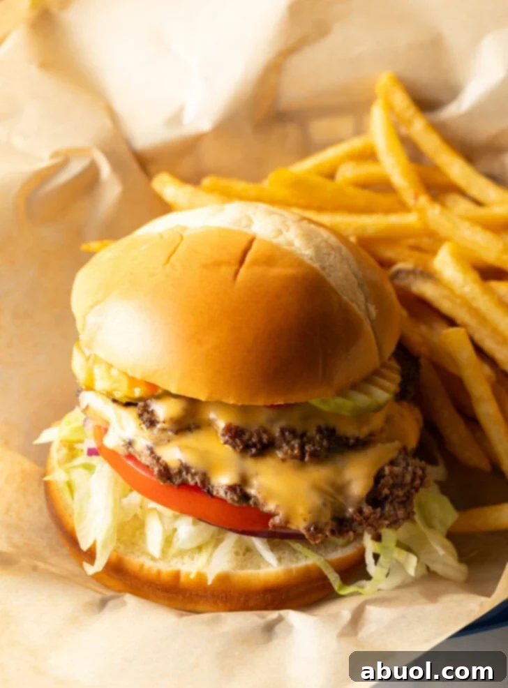 Double patty smash burger with cheese, shredded lettuce, and tomato. Next the burger is a side of french fries.