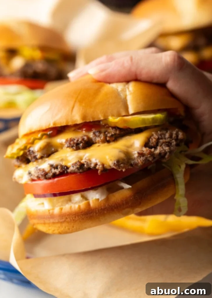 Hand holding double patty smash burger with cheese, shredded lettuce, and tomato.