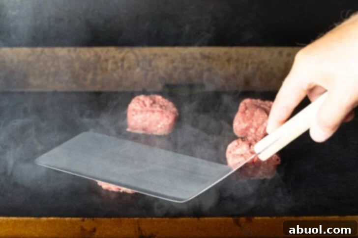 Large metal spatula smooshing a hamburger patty on a blackstone grill.
