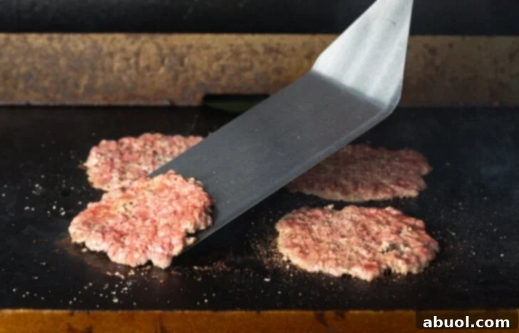 Large metal spatula flipping a hamburger patty on a blackstone grill.